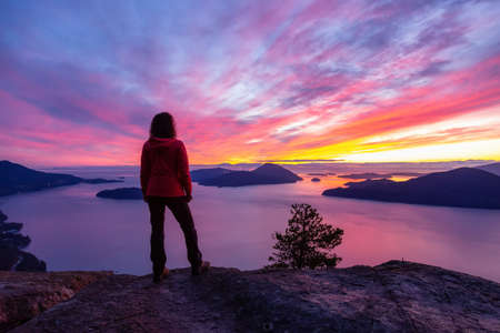 Adventurous Caucasian Girl standing on top of a mountain during a colorful winter sunset. Taken on Tunnel Bluffs Hike, North of Vancouver, BC, Canada.の写真素材