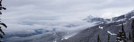 Whistler, British Columbia, Canada. Beautiful Panoramic View of the Canadian Snow Covered Mountain Landscape during a cloudy and foggy winter day.の写真素材