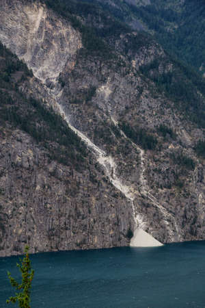 Landslide off a rocky mountain into Anderson Lake during a cloudy summer day. Located near Lillooet,...