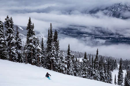 Whistler, British Columbia, Canada. Beautiful View of the Canadian Snow Covered Mountain Landscape with Man Skiing down the run during a cloudy and foggy winter day.の写真素材