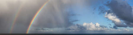 Dramatic Panoramic View of a cloudscape during a rainy and colorful morning with a bright double Rainbow. Taken over the Pacific Ocean in Alaska, USA.の写真素材