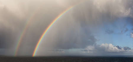 Dramatic Panoramic View of a cloudscape during a rainy and colorful morning with a bright double Rainbow. Taken over the Pacific Ocean in Alaska, USA.の写真素材