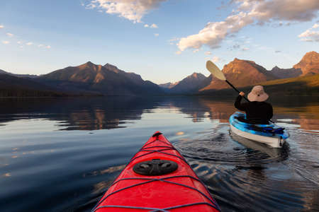 Adventurous Man Kayaking in Lake McDonald during a sunny summer sunset with American Rocky Mountains...