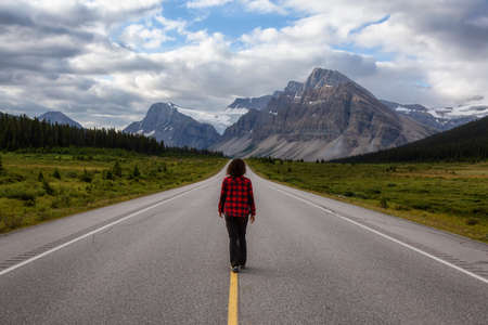 Girl walking down a scenic road in the Canadian Rockies during a vibrant summer morning. Taken in Icefields Parkway, Banff National Park, Alberta, Canada.の写真素材