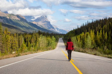 Girl walking down a scenic road in the Canadian Rockies during a vibrant summer morning. Taken in...