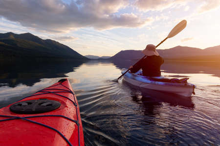 Adventurous Man Kayaking in Lake McDonald during a sunny summer sunset with American Rocky Mountains in the background. Taken in Glacier National Park, Montana, USA.の写真素材