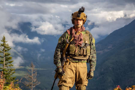 Chilliwack, British Columbia, Canada - October 5, 2019: Army Man wearing Tactical Uniform and holding Machine gun in the Outdoor Mountains during fall season.のeditorial素材