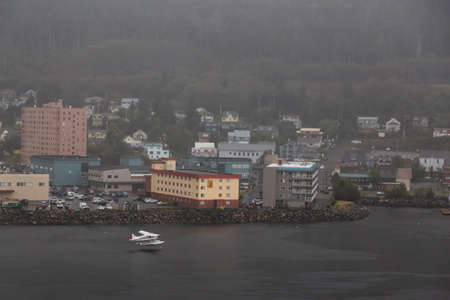 Ketchikan, Alaska, United States - September 26, 2019: Beautiful Aerial View of an Airplane Landing on water in front of a small touristic town in the Ocean Coast during a stormy and rainy morning.のeditorial素材