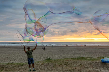 Seaside, Oregon, USA - September 6, 2019: Man making big Soap Bubbles on the sandy beach during a...