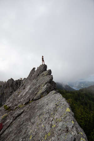 Adventurous Girl on top of a rugged rocky mountain during a cloudy summer morning. Taken on Crown Mountain, North Vancouver, BC, Canada.の写真素材