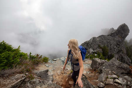 Adventurous Girl is hiking up a steep trail up a beautiful rocky mountain during a cloudy summer...