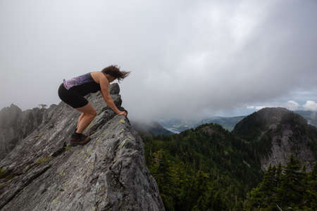 Adventurous Girl on top of a rugged rocky mountain during a cloudy summer morning. Taken on Crown Mountain, North Vancouver, BC, Canada.の写真素材