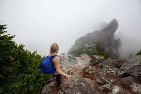 Adventurous Girl is hiking up a steep trail up a beautiful rocky mountain during a cloudy summer morning. Taken on Crown Mountain, North Vancouver, BC, Canada.の写真素材