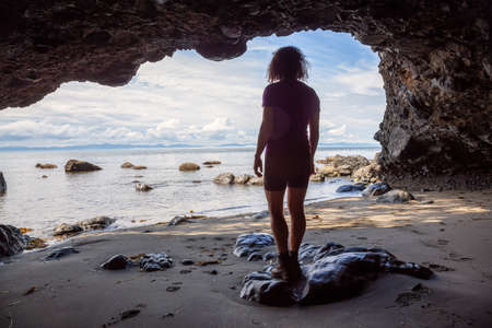 Adventurous girl hiking in a cave on Juan de Fuca Trail to Mystic Beach on the Pacific Ocean Coast during a sunny summer day. Taken near Port Renfrew, Vancouver Island, BC, Canada.の写真素材