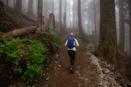 Adventurous girl hiking on a trail in the woods during a foggy and rainy day. Taken in Cypress Provincial Park, Vancouver, British Columbia, Canada.の写真素材