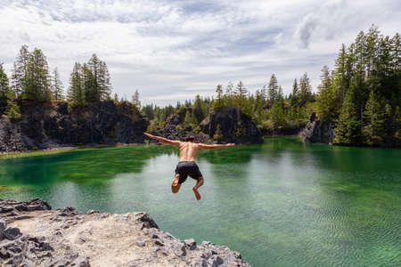 Athletic and Adventurous Man is Cliff Jumping into a Green Colored Glacier Lake during a hot and sunny summer day. Taken in British Columbia, Canada.の写真素材
