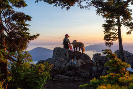 Adventurous Girl is hiking with a dog on top of St. Mark's Mountain during a sunny summer sunset. Located in West Vancouver, British Columbia, Canada.の写真素材