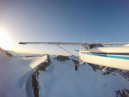 Small airplane flying near the rocky Canadian Mountains during a vibrant summer sunset. Taken near...