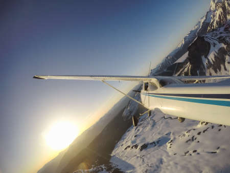 Small airplane flying near the rocky Canadian Mountains during a vibrant summer sunset. Taken near...