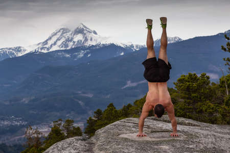 Fit and Muscular Young Man is doing exercises on top of the Mountain during a cloudy day. Taken on...