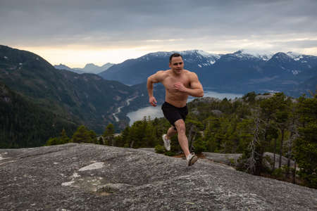 Fit and Muscular Young Man is Running up the Mountain during a cloudy sunset. Taken on Chief Mountain in Squamish, North of Vancouver, BC, Canada.の写真素材