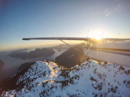 Small airplane flying near the rocky Candian Mountains during a vibrant sunset. Taken near Squamish, North of Vancouver, British Columbia, Canada.の写真素材