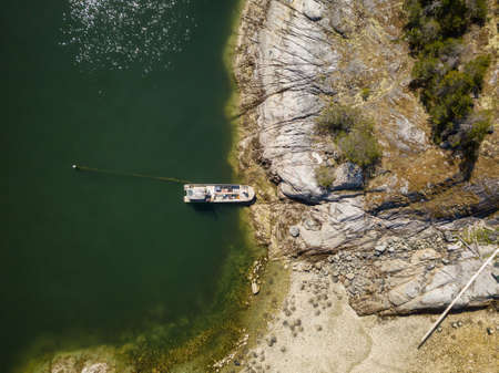 Aerial view from above of a fishing boat parked on a rocky island during a sunny summer day. Taken near Powell River, Sunshine Coast, British Columbia, Canada.の写真素材