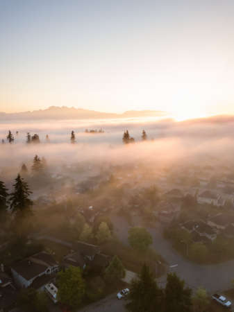 Aerial view of a residential neighborhood covered in a layer of fog during a vibrant sunrise. Taken in Greater Vancouver, BC, Canada.の写真素材