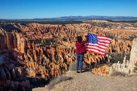 Woman holding a flag enjoying the Beautiful View of an American landscape during a sunny day. Taken in Bryce Canyon National Park, Utah, United States of America.の写真素材