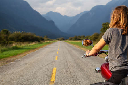 Woman riding a motorcycle on a scenic road surrounded by Canadian Mountains. Taken in Pitt Meadows, Greater Vancouver, BC, Canada.の写真素材