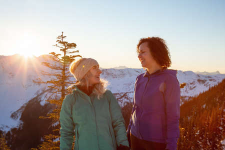 Couple friends are socializing on top of a mountain during a vibrant winter sunset. Taken on top of Zoa Peak near Hope, British Columbia, Canada.の写真素材