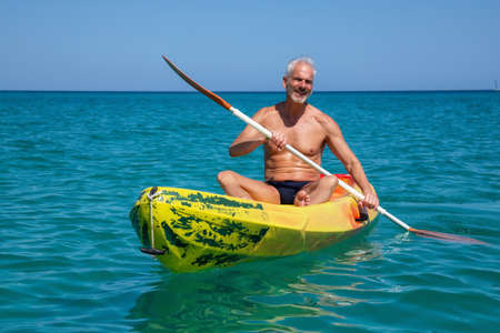 Elder fit man is kayaking on a bright yellow kayak in Caribbean Sea during a sunny summer day. Taken in Varadero, Cuba.の写真素材