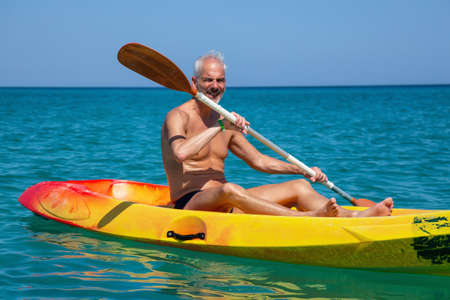 Elder fit man is kayaking on a bright yellow kayak in Caribbean Sea during a sunny summer day. Taken in Varadero, Cuba.の写真素材