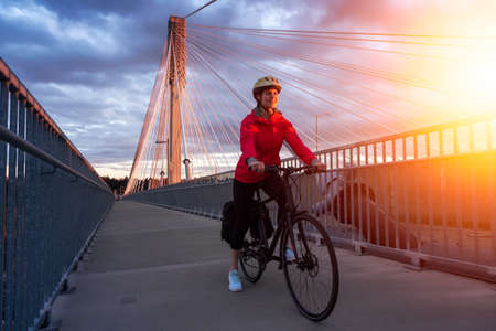 Caucasian Woman riding a Bicycle on a path at Port Mann Bridge during vibrant Sunset. Taken in Surrey, Vancouver, British Columbia, Canada.の写真素材