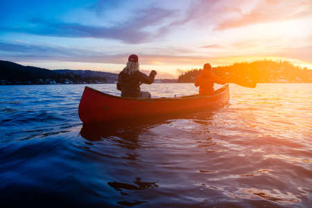 Couple friends on a wooden canoe are paddling in water during a vibrant sunny sunset. Taken in Indian Arm, near Deep Cove, North Vancouver, British Columbia, Canada. Concept: Adventure, Sport, Exploreの写真素材