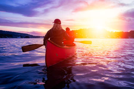 Couple friends on a wooden canoe are paddling in water during a vibrant sunny sunset. Taken in Indian Arm, near Deep Cove, North Vancouver, British Columbia, Canada. Concept: Adventure, Sport, Exploreの写真素材