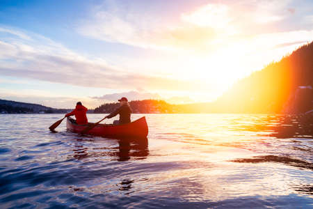 Couple friends on a wooden canoe are paddling in water during a vibrant sunny sunset. Taken in Indian Arm, near Deep Cove, North Vancouver, British Columbia, Canada. Concept: Adventure, Sport, Exploreの写真素材