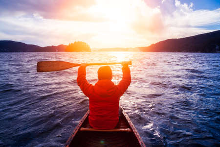 Man with Hand Up on wooden canoe are paddling in water during a vibrant sunny day. Taken in Indian...