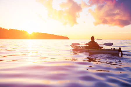 Woman on a sea kayak is paddling in the ocean during a colorful and vibrant sunset. Taken in Jericho, Vancouver, British Columbia, Canada. Concept: Adventure, Holiday, Vacation, Lifestyle, Freedomの写真素材