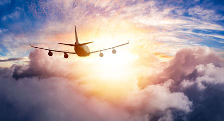 Aerial View of Commercial Airliner Jet Plane Flying in above the clouds during a colorful sunset or...