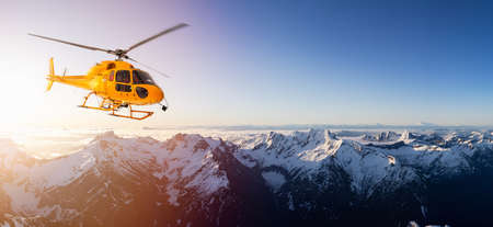 Yellow Helicopter flying over the Rocky Mountains during a sunny sunset. Aerial Landscape from British Columbia, Canada near Vancouver. Composite. Canadian Panoramic Nature Backgroundの写真素材