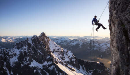 Epic Adventure Extreme Sport Composite of Rock Climbing Man Rappelling from a Cliff. Mountain Landscape Background from British Columbia, Canada.の写真素材