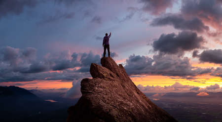 Magical Fantasy Adventure Composite of Man Hiking on top of a rocky mountain peak. Background Landscape from British Columbia, Canada. Sunset or Sunrise Dramatic Colorful Skyの写真素材