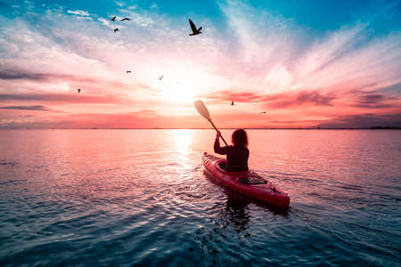 Sea Kayaking in calm waters during a colorful and vibrant sunset. Adventure Girl in Red Kayak. Location: White Rock, Vancouver, British Columbia, Canada.の写真素材
