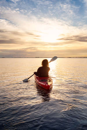 Sea Kayaking in calm waters during a colorful and vibrant sunset. Adventure Girl in Red Kayak....