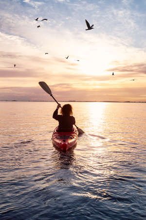 Sea Kayaking in calm waters during a colorful and vibrant sunset. Adventure Girl in Red Kayak. Location: White Rock, Vancouver, British Columbia, Canada.の写真素材