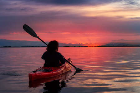 Sea Kayaking in calm waters during a colorful and vibrant sunset. Adventure Girl in Red Kayak....