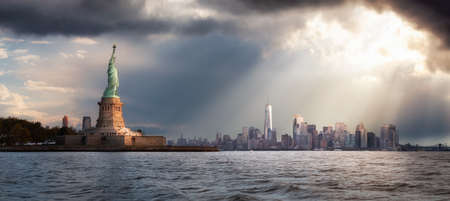 Panoramic view of the Statue of Liberty and Downtown Manhattan in the background during a vibrant cloudy sunrise. Taken in New York City, NY, United States.の写真素材