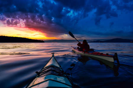 Adventure Man on a Sea Kayak is kayaking during a vibrant and colorful winter sunset. Taken in Vancouver, British Columbia, Canada. Adventure, Vacation Conceptの写真素材