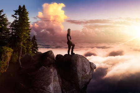 Girl Hiking on on a Rocky Mountain Peak with Beautiful and striking view of the puffy clouds during a colorful and vibrant sunset or sunrise. Artistic Composite. Freedom, Lifestyle, Adventureの写真素材